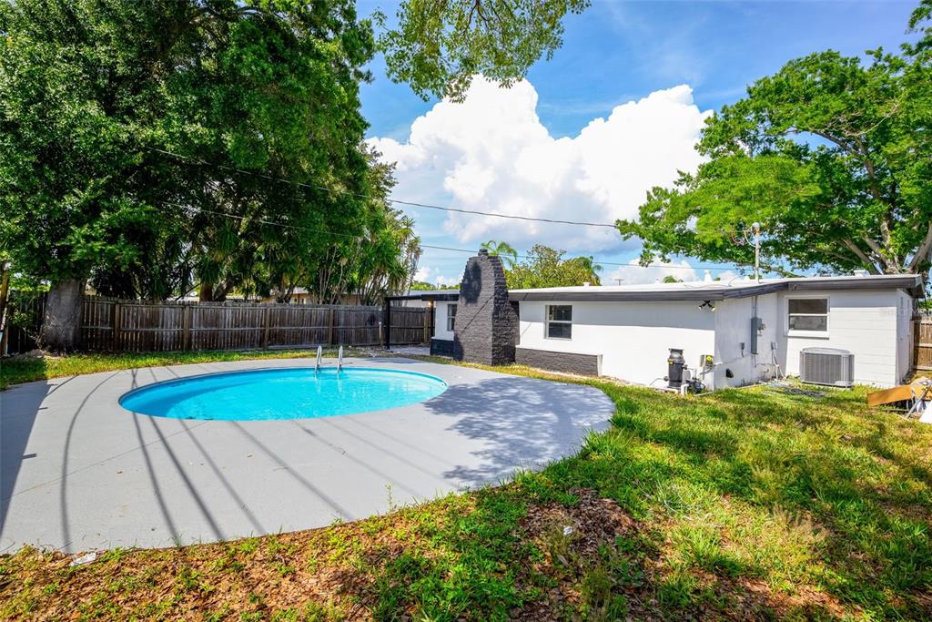 A backyard features a swimming pool, a gray concrete deck, and a white house exterior — 9596 GROVELAND STREET, SEMINOLE, FL