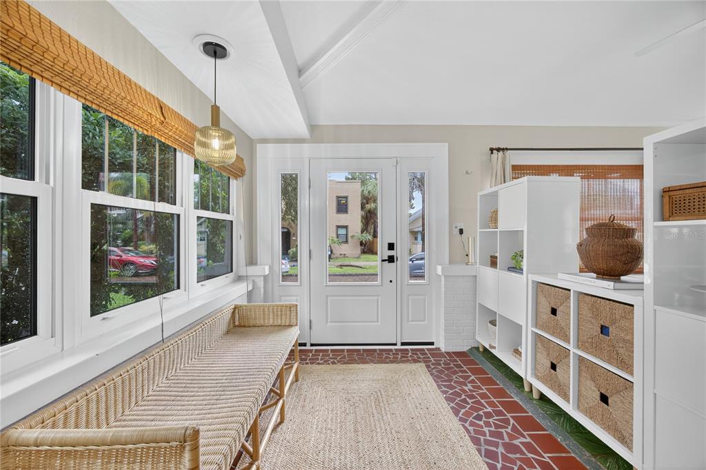 A sunroom features a red tile floor, a wicker bench, and a white front door — 221 13TH AVENUE NE, ST PETERSBURG, FL