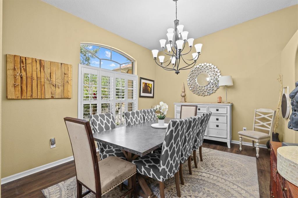 A dining room features a metal-topped table, patterned chairs, a chandelier, and a white sideboard — 8331 GOLDEN PRAIRIE DRIVE, TAMPA, FL