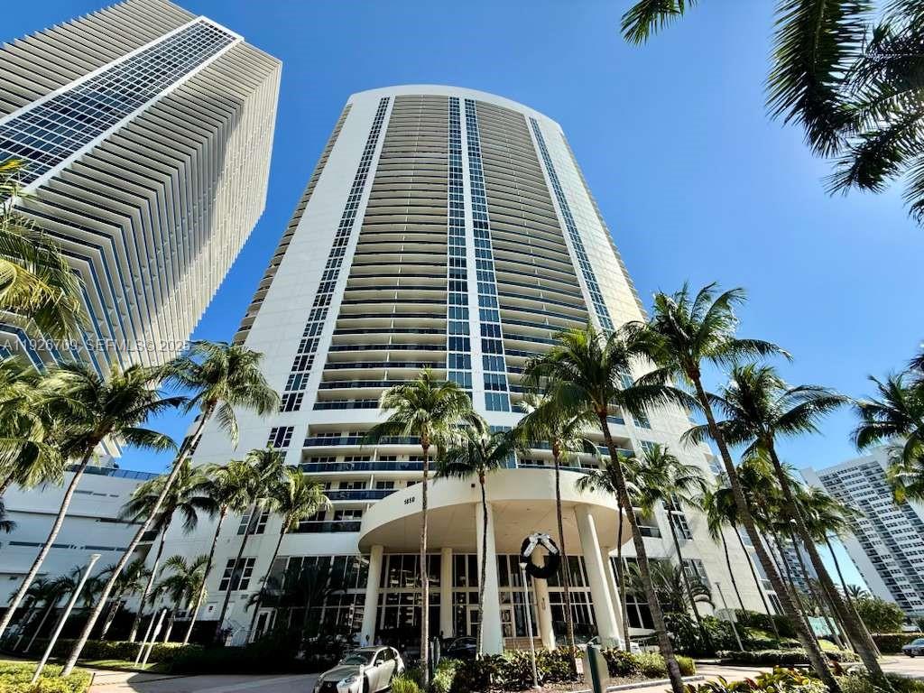 A low-angle view of a tall white residential skyscraper surrounded by palm trees — 1850 S Ocean Dr # 1405, Hallandale Beach FL 33009, HALLANDALE BEACH, FL