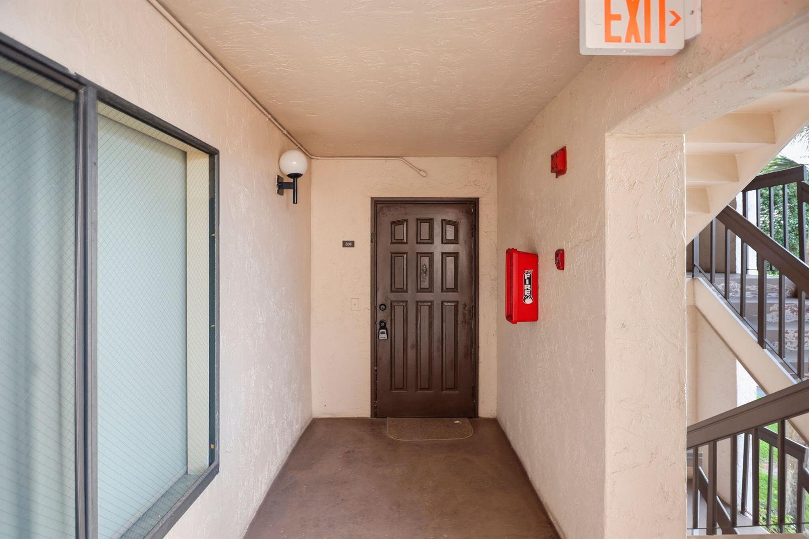 An exterior view of a brown apartment door with a red fire extinguisher box nearby — 10110 Cedar Point Boulevard # 206, Boynton Beach FL 33437, BOYNTON BEACH, FL