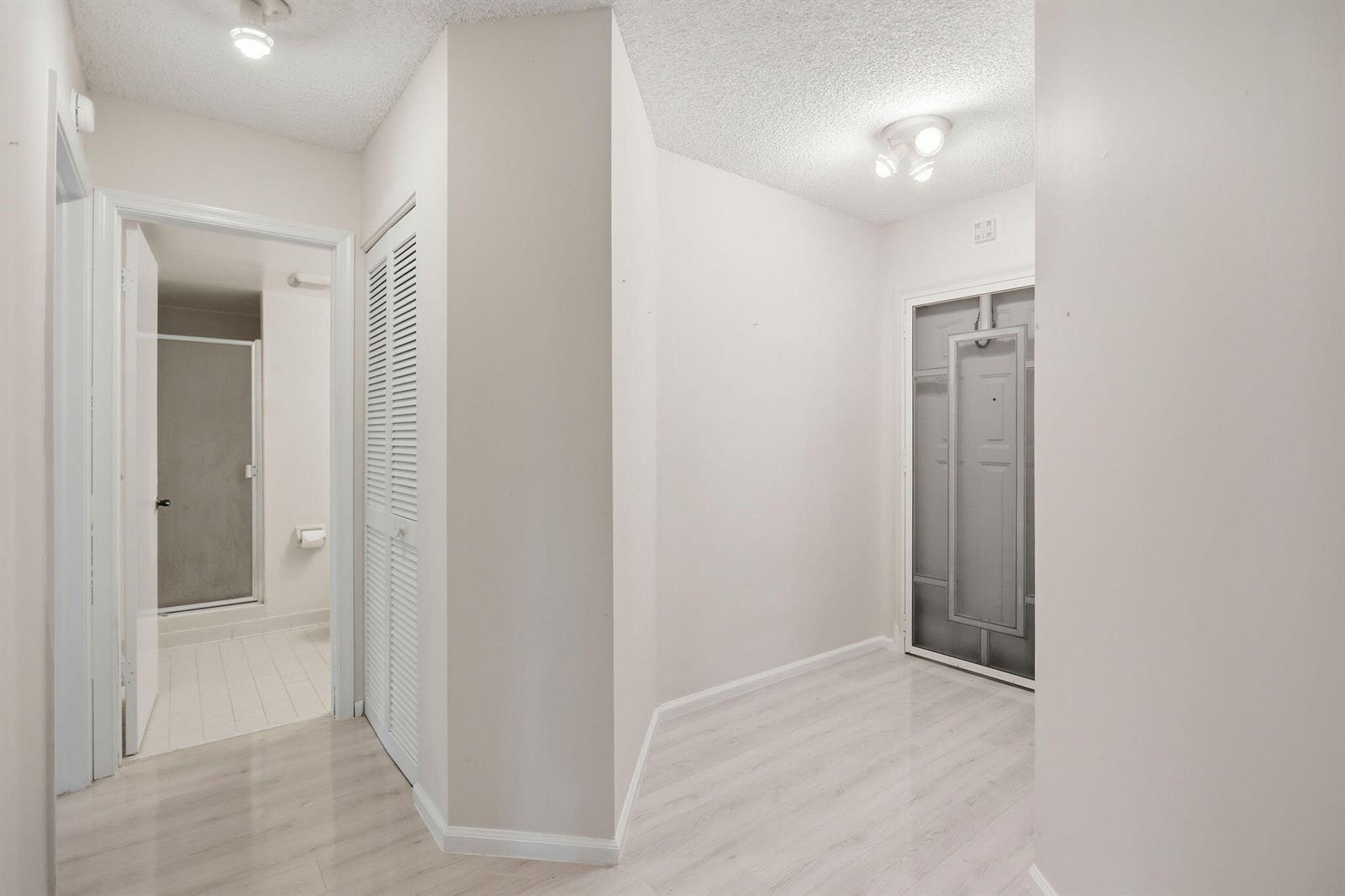 A hallway with light wood-look flooring, white walls, a closet, and a bathroom entrance — 10110 Cedar Point Boulevard # 206, Boynton Beach FL 33437, BOYNTON BEACH, FL