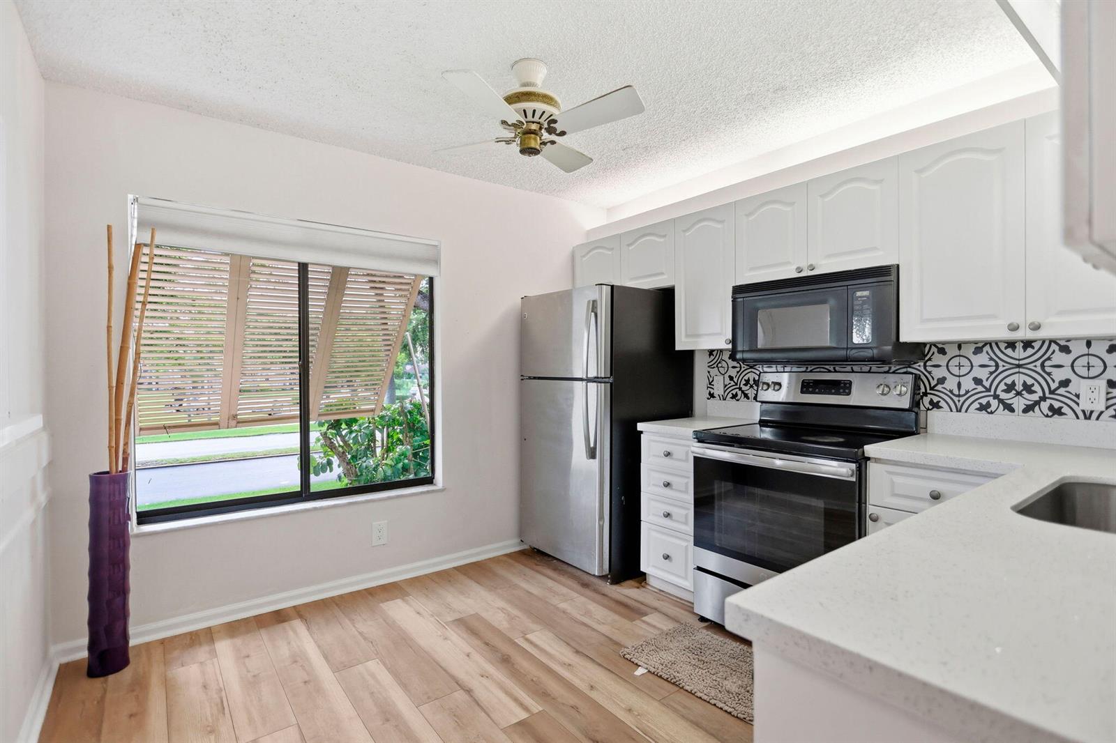 A kitchen features white cabinets, stainless steel appliances, patterned backsplash, and light wood-look flooring — 10110 Cedar Point Boulevard # 206, Boynton Beach FL 33437, BOYNTON BEACH, FL