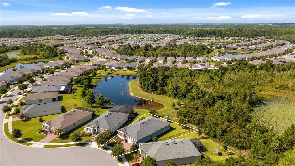 An aerial view shows a suburban neighborhood with houses, a pond, and wooded areas — 3899 WINGED ELM COURT, CLERMONT, FL
