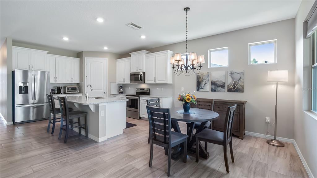 A kitchen and dining area with white cabinets, stainless steel appliances, and wood-look tile flooring — 3899 WINGED ELM COURT, CLERMONT, FL