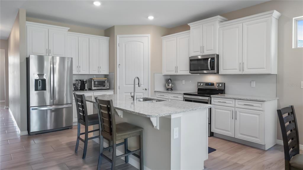 A kitchen with white cabinets, stainless steel appliances, a center island, and wood-look tile flooring — 3899 WINGED ELM COURT, CLERMONT, FL