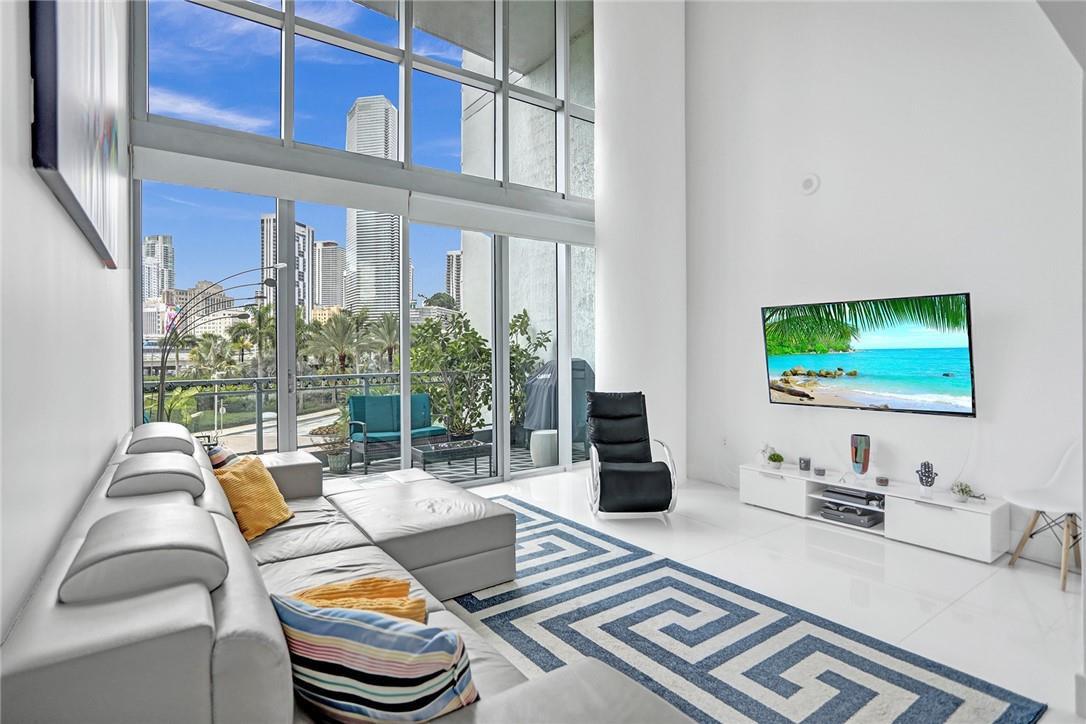 A modern kitchen with dark cabinets and a white island opens into a living area — 90 SW 3rd Street, Miami FL 33130, MIAMI, FL