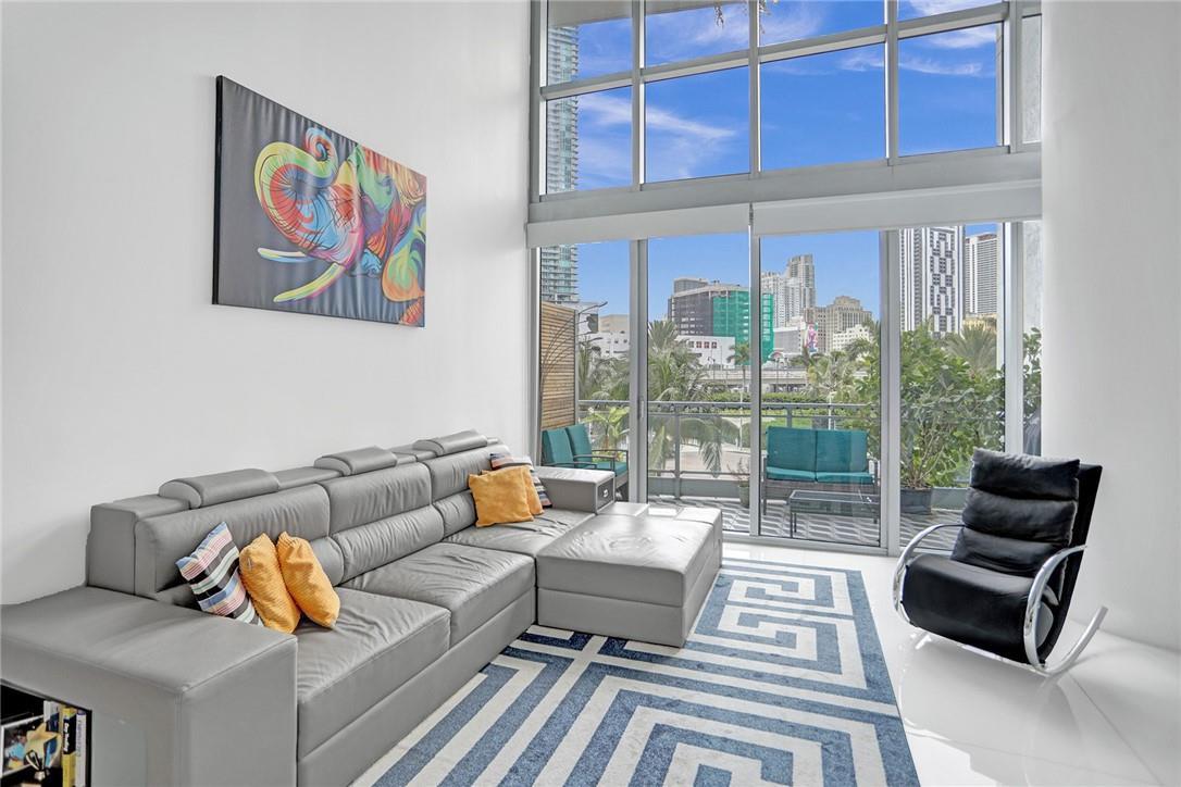 A high-angle view of a modern living room with a gray sectional, balcony, and artwork — 90 SW 3rd Street, Miami FL 33130, MIAMI, FL