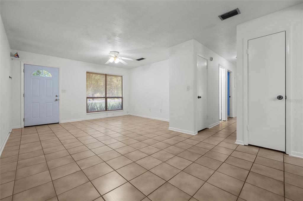 An empty room with light-colored tile flooring, white walls, a ceiling fan, and a front door — 4219 NW 30TH TERRACE, GAINESVILLE, FL