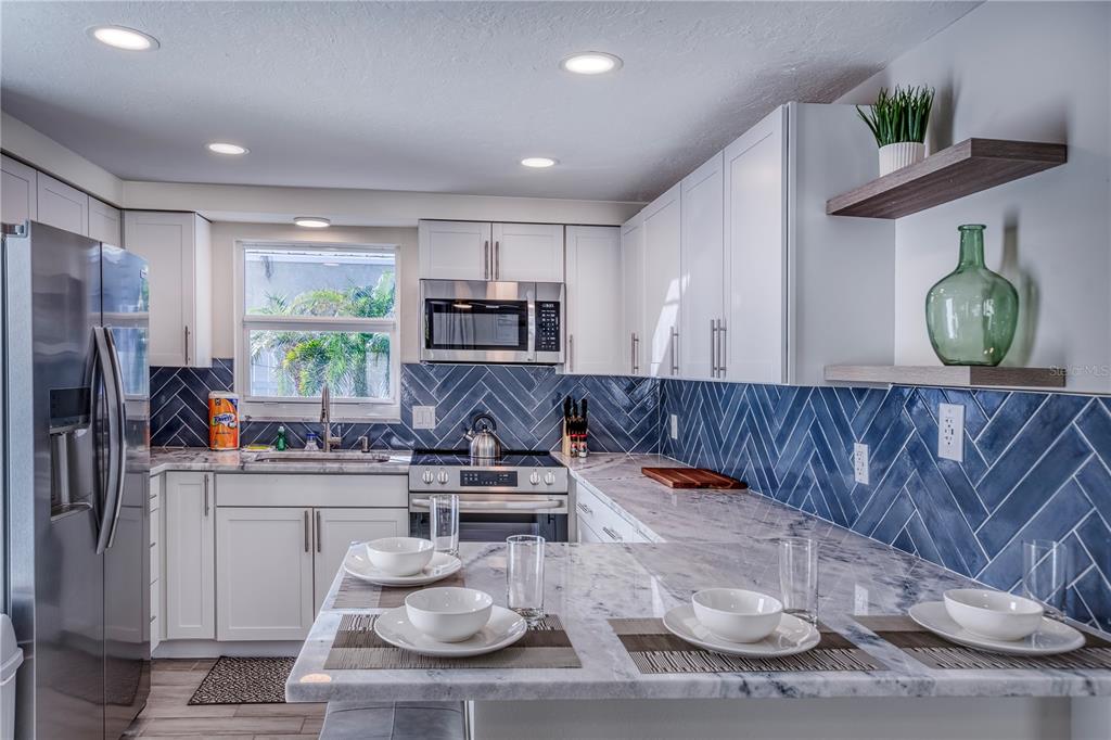 A kitchen features white cabinets, marble countertops, and a blue herringbone tile backsplash — 3604 GULF DRIVE UNIT A and B, HOLMES BEACH, FL