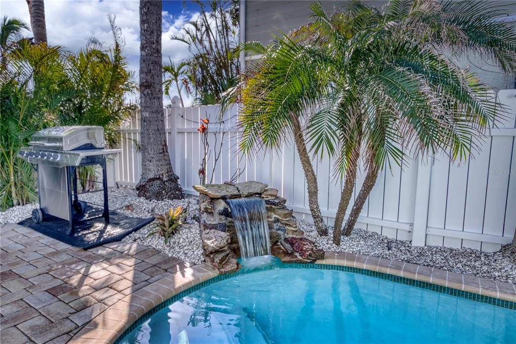 A backyard pool area features a stone waterfall, a grill, and a white privacy fence — 3604 GULF DRIVE UNIT A and B, HOLMES BEACH, FL
