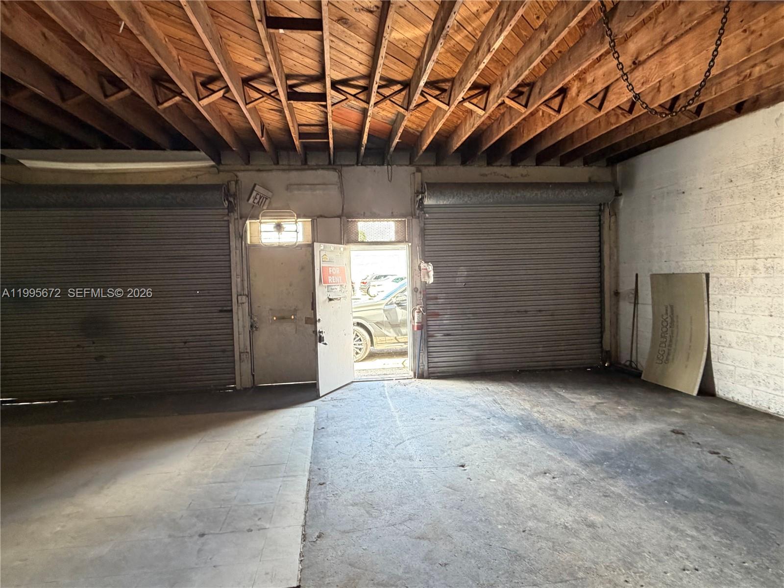 An industrial space features exposed wooden ceiling joists, concrete floors, and two metal roll-up doors — 1017 N 20th Ave, Hollywood FL 33020, HOLLYWOOD, FL