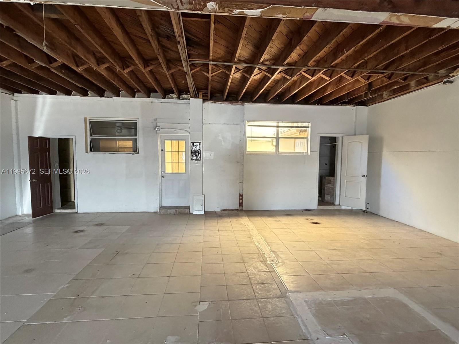 An unfinished room features exposed wooden ceiling joists, tiled flooring, and multiple doorways — 1017 N 20th Ave, Hollywood FL 33020, HOLLYWOOD, FL