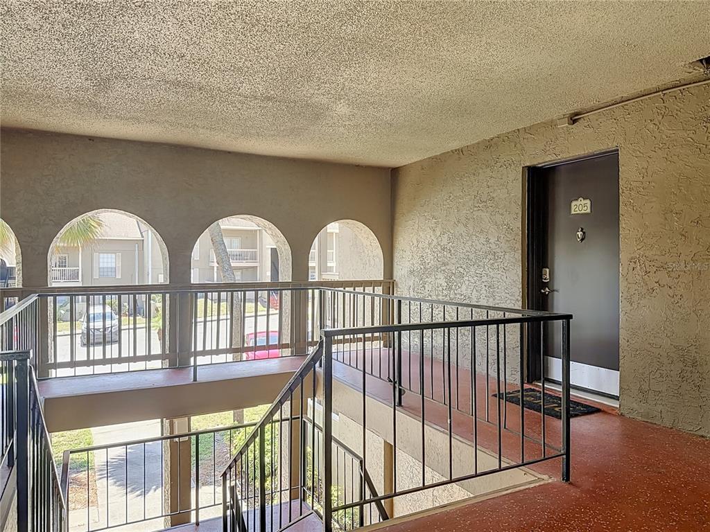 An outdoor apartment hallway features arched openings, metal railings, and a door labeled 205 — 305 WYMORE ROAD UNIT 205, ALTAMONTE SPRINGS, FL