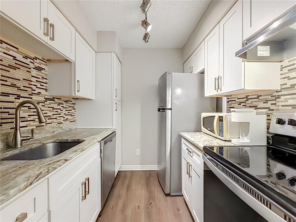 A galley kitchen features white cabinets, stainless steel appliances, granite countertops, and a tiled backsplash — 305 WYMORE ROAD UNIT 205, ALTAMONTE SPRINGS, FL