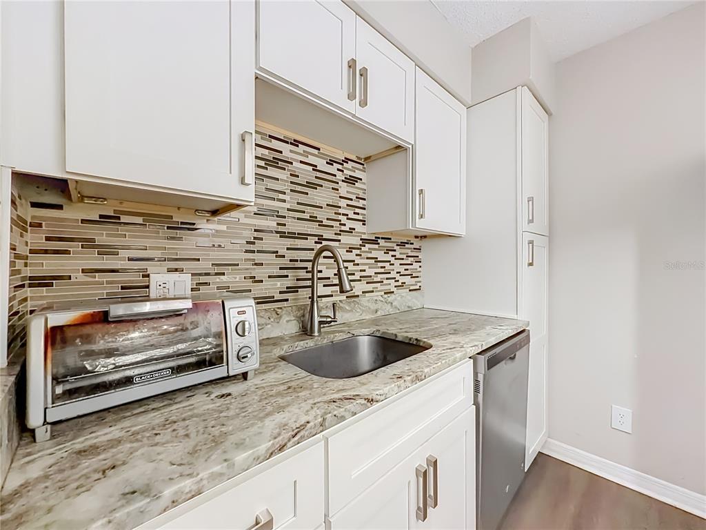 A kitchen features white cabinets, granite countertops, a stainless steel sink, and a tiled backsplash — 305 WYMORE ROAD UNIT 205, ALTAMONTE SPRINGS, FL