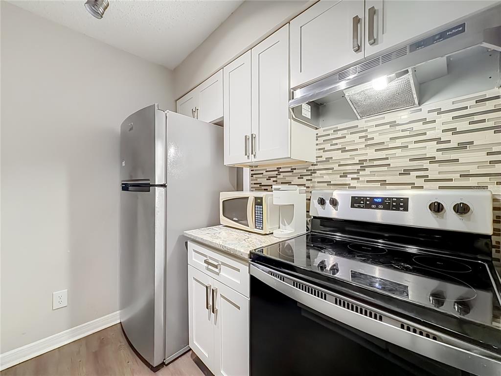 A kitchen features white cabinets, stainless steel appliances, and a tiled backsplash — 305 WYMORE ROAD UNIT 205, ALTAMONTE SPRINGS, FL