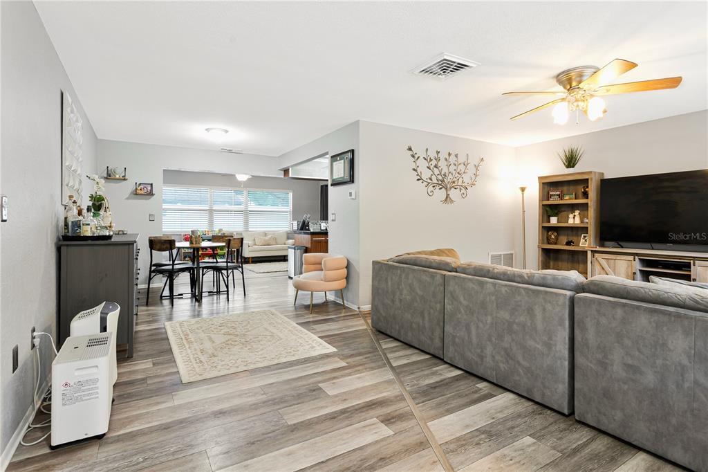 A living room with gray wood-look flooring, a large sectional sofa, and an open dining area — 182 SUNWARD AVENUE, PALM HARBOR, FL