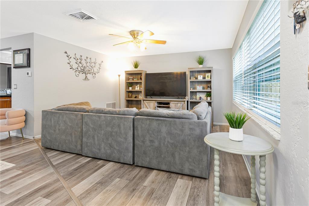 A living room features a gray sectional sofa, a television console, and wood-look flooring — 182 SUNWARD AVENUE, PALM HARBOR, FL