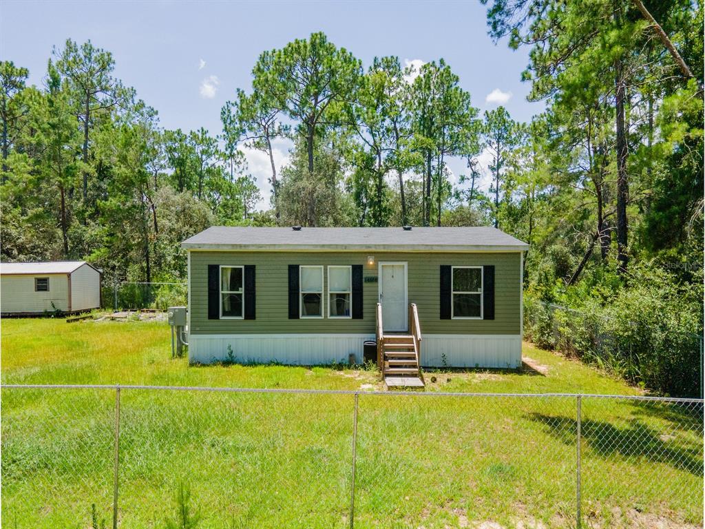 A single-story manufactured home with green siding stands in a grassy lot with pine trees — 14668 NE 204TH PLACE, FORT MC COY, FL