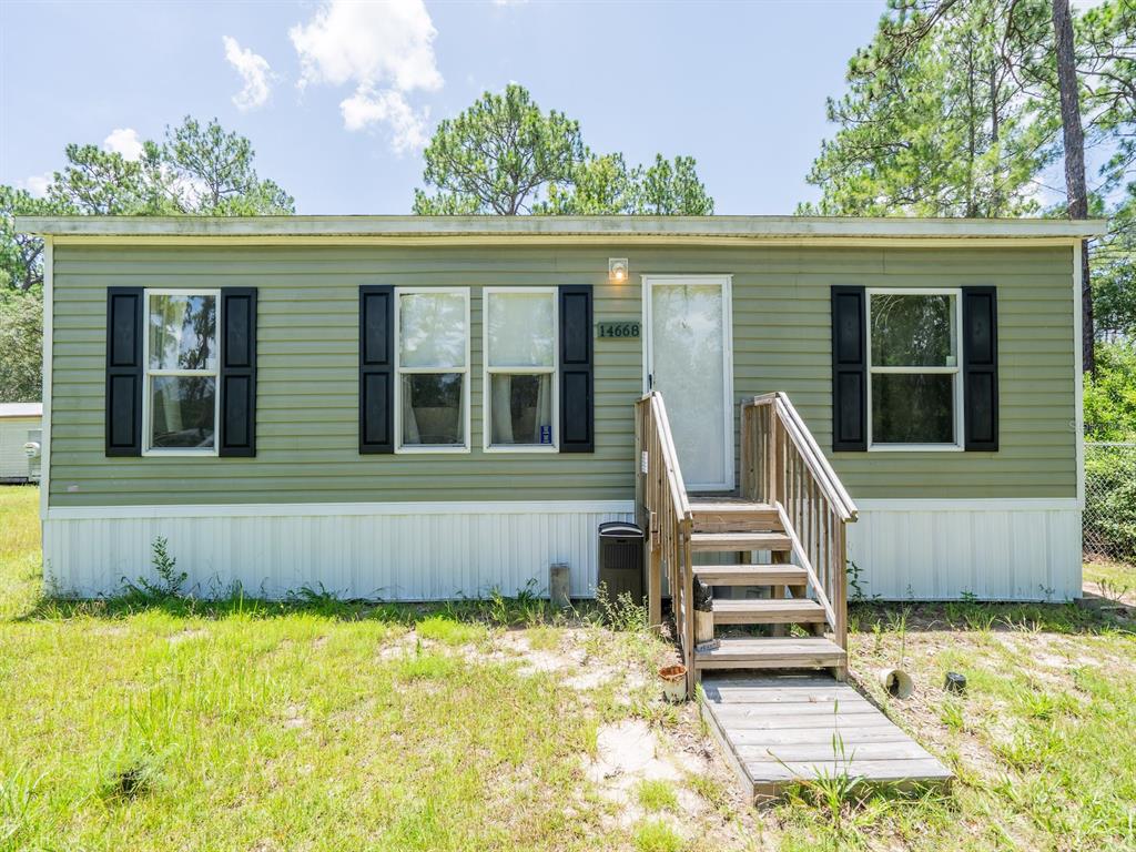 A green manufactured home with black shutters and wooden stairs sits on a grassy lot — 14668 NE 204TH PLACE, FORT MC COY, FL
