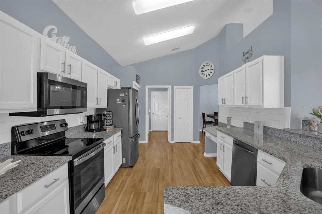 A kitchen features white cabinets, granite countertops, stainless steel appliances, and light wood flooring — 116 FLEMING LANE, DAVENPORT, FL