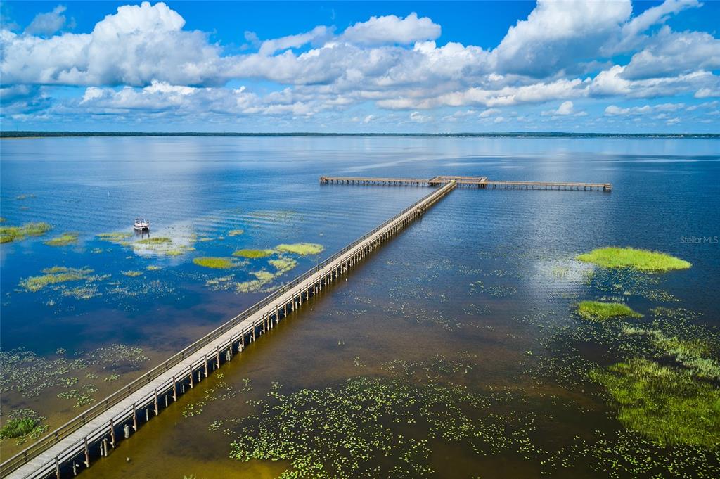 An aerial view shows a long wooden pier extending into a large, calm lake — 913 INDIAN LAKE DRIVE, INDIAN LAKE ESTATES, FL