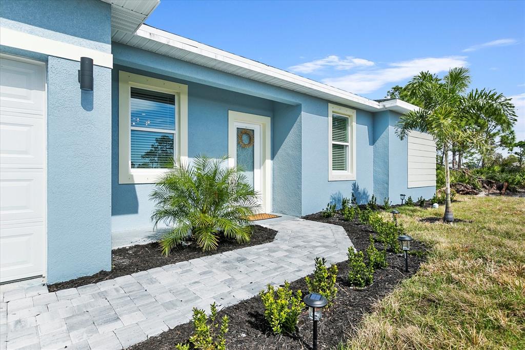 A light blue house exterior features a paved walkway leading to the front entrance — 18400 TULANE AVENUE, PORT CHARLOTTE, FL