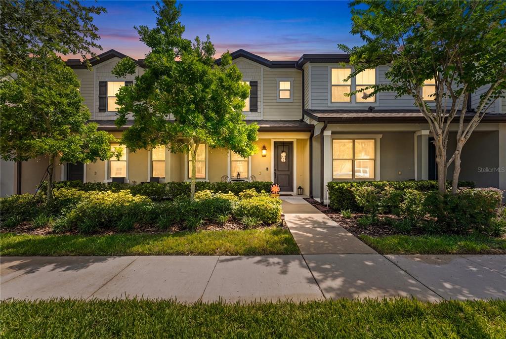 A two-story townhouse exterior features a light-colored facade, a front walkway, and mature landscaping — 5033 CASPIAN STREET, ST CLOUD, FL