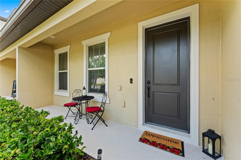 A covered front porch features a dark gray door, two chairs, a small table, and landscaping — 5033 CASPIAN STREET, ST CLOUD, FL
