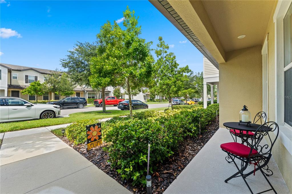 A covered front porch features a small bistro set overlooking a landscaped yard and street — 5033 CASPIAN STREET, ST CLOUD, FL