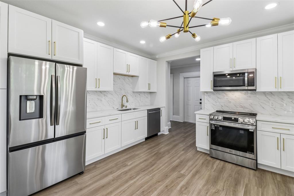 A modern kitchen features white cabinets, stainless steel appliances, and marble-patterned countertops and backsplash — 43 W MURIEL STREET, ORLANDO, FL