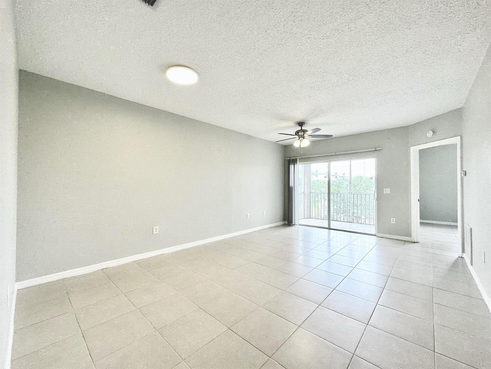 An empty living room features light gray walls, tile flooring, a ceiling fan, and a balcony — 9604 Seadale Court # 201, Riverview FL 33578, RIVERVIEW, FL