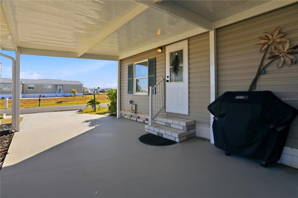 A covered concrete patio features a white front door, steps, and a covered grill — 1427 SANDERLING DRIVE, ENGLEWOOD, FL