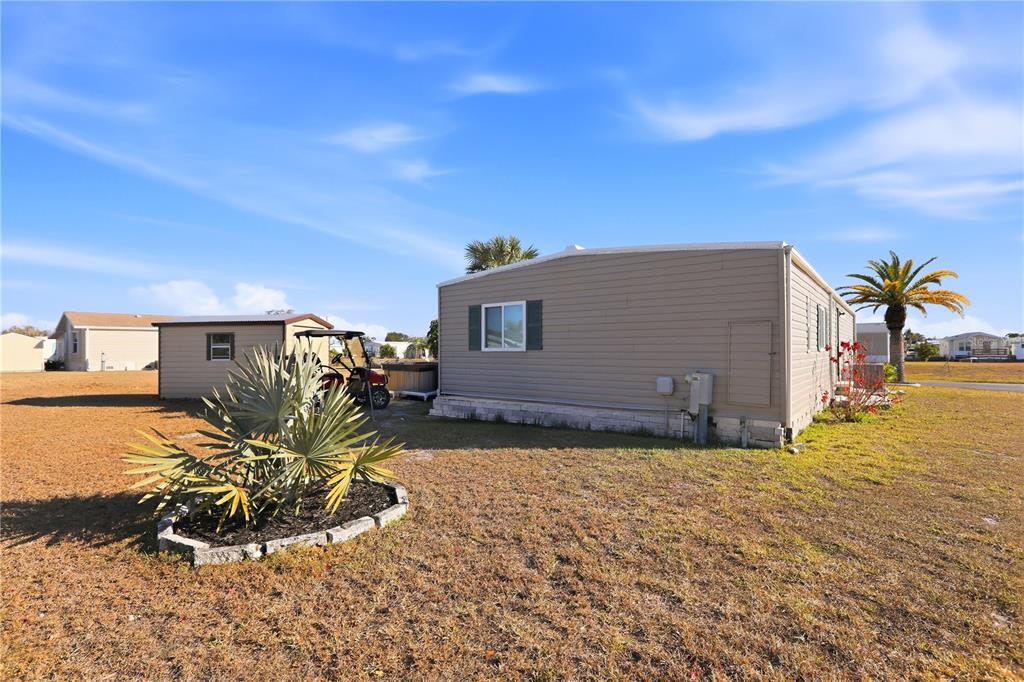 A tan mobile home with a small shed, golf cart, and palm tree on grass — 1427 SANDERLING DRIVE, ENGLEWOOD, FL