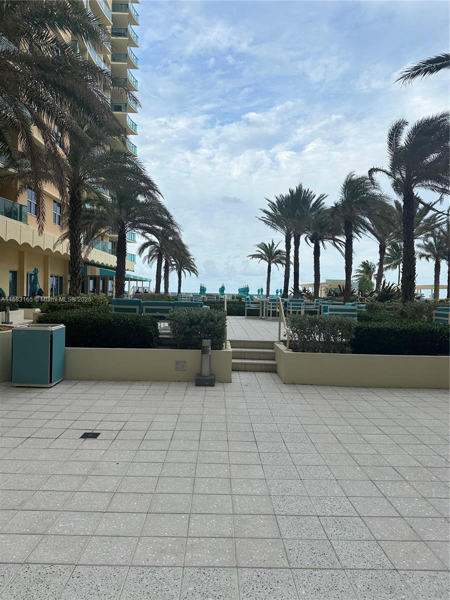 A paved outdoor patio features palm trees, seating areas, and steps leading toward the ocean — 2501 S Ocean Dr # 1530, Hollywood FL 33019, HOLLYWOOD, FL