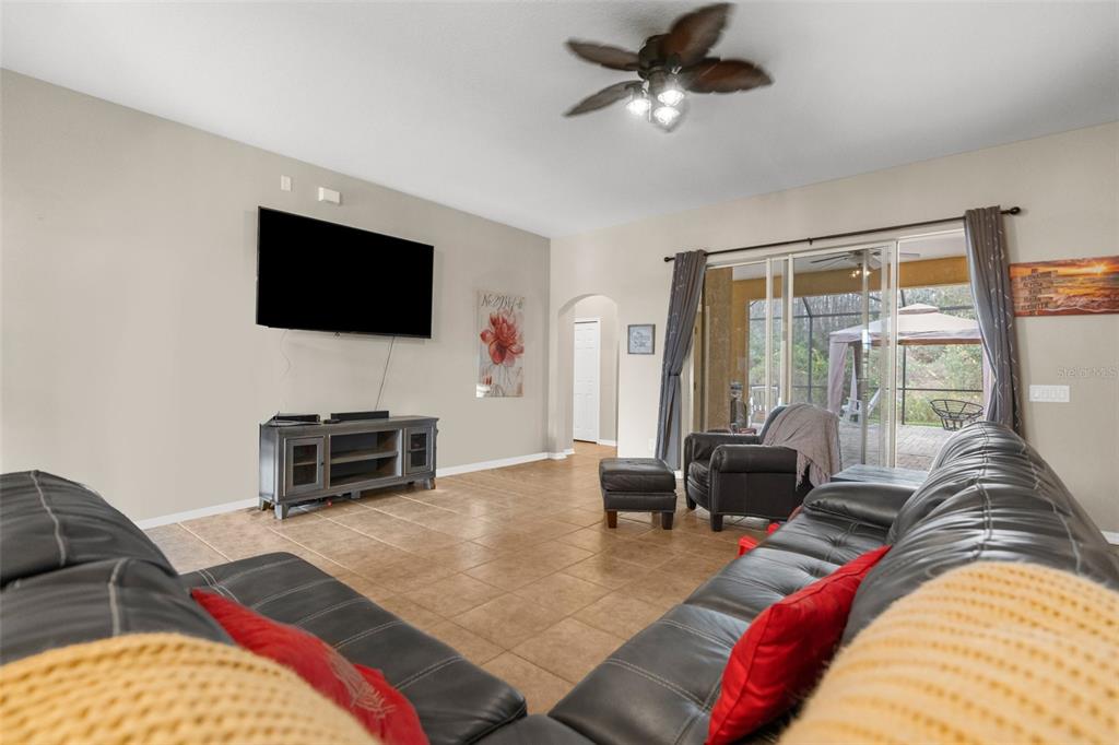 A living room features tile flooring, a mounted television, leather furniture, and a sliding glass door — 19200 SUNSET BAY DRIVE, LAND O LAKES, FL