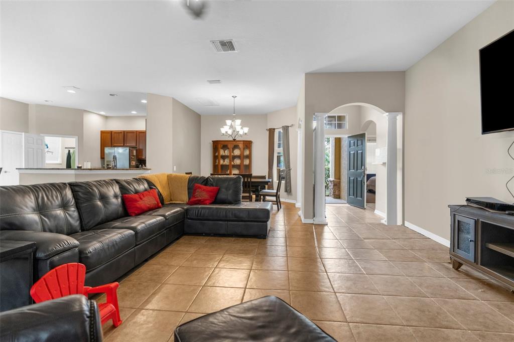 A living room with tile floors, a large black sectional sofa, and an arched entryway — 19200 SUNSET BAY DRIVE, LAND O LAKES, FL