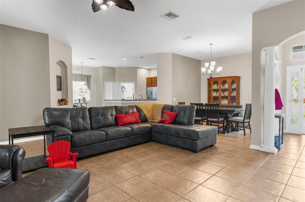A living room with a large sectional sofa, tile floors, and an adjacent dining area — 19200 SUNSET BAY DRIVE, LAND O LAKES, FL