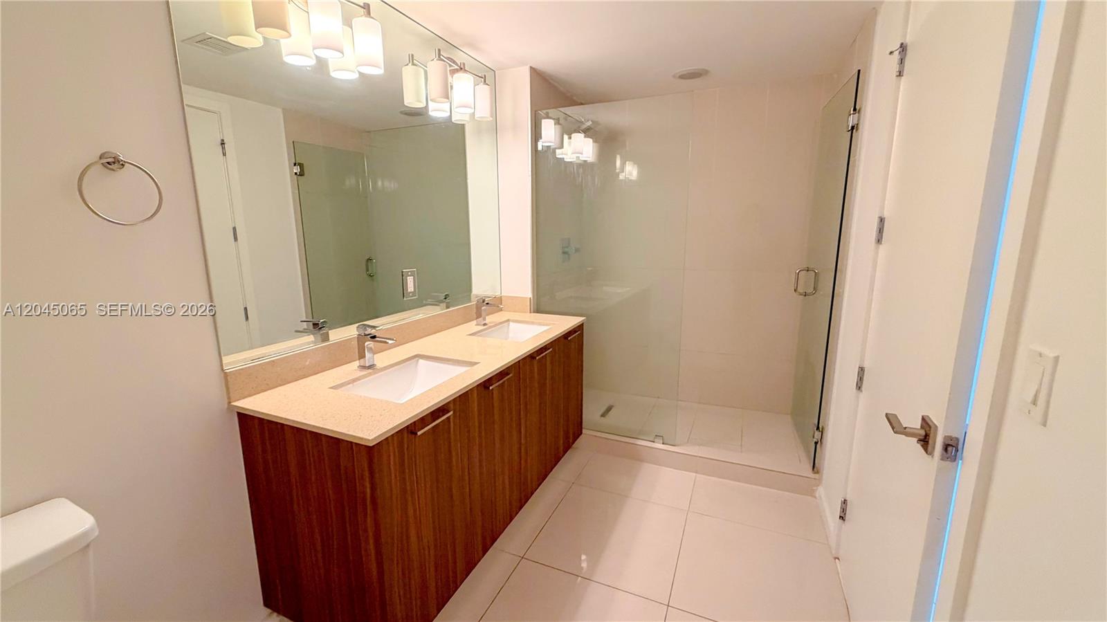 This bathroom features a double vanity with wood cabinets, a large mirror, and a glass-enclosed shower — DORAL, FL