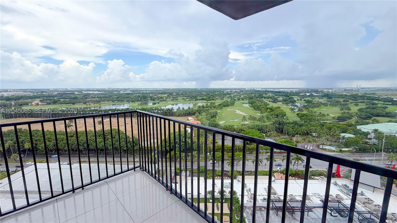 A high-rise balcony with a black metal railing overlooks a golf course and road — DORAL, FL