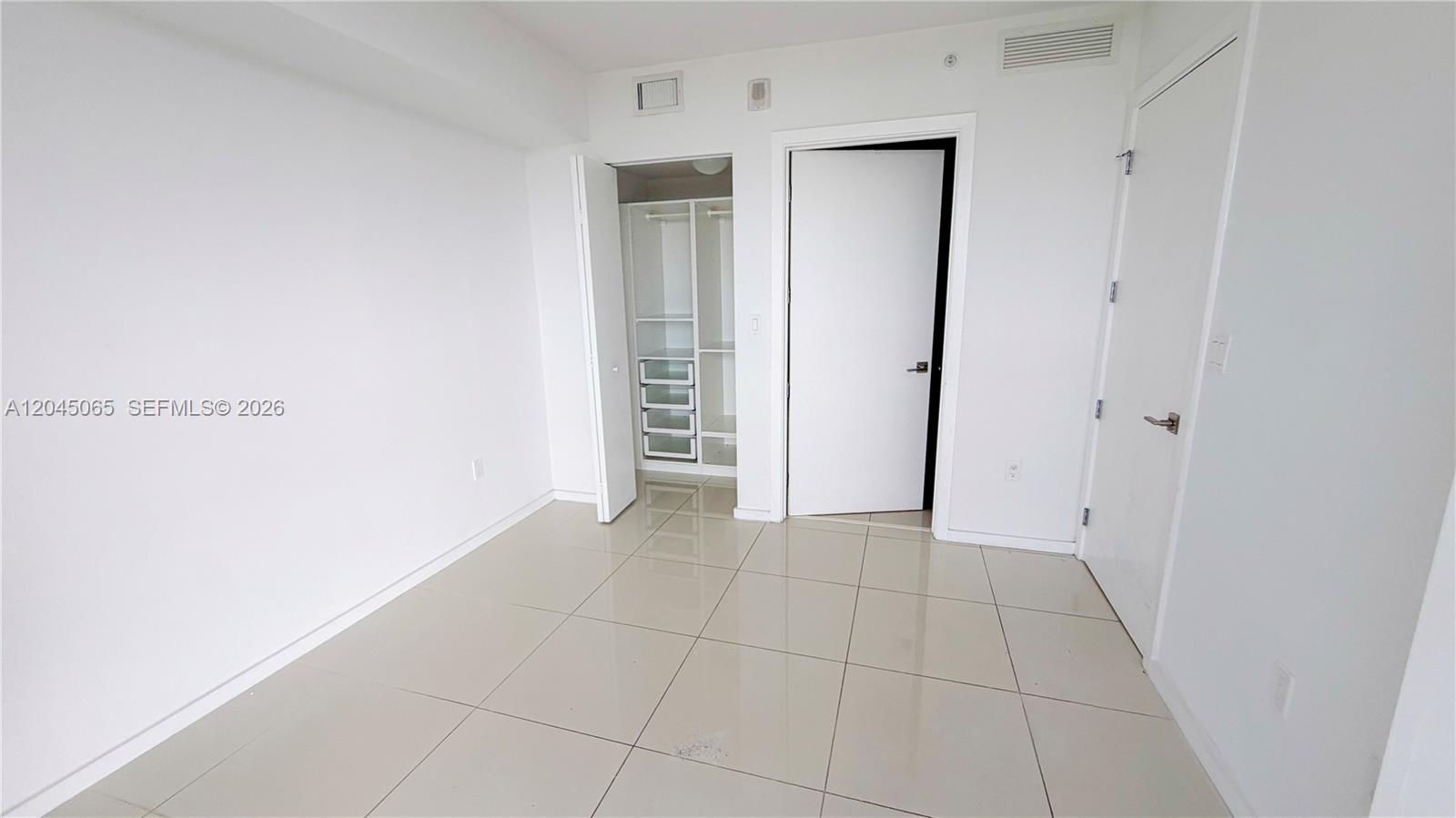 An empty room features white walls, large beige floor tiles, a walk-in closet, and two doors — DORAL, FL