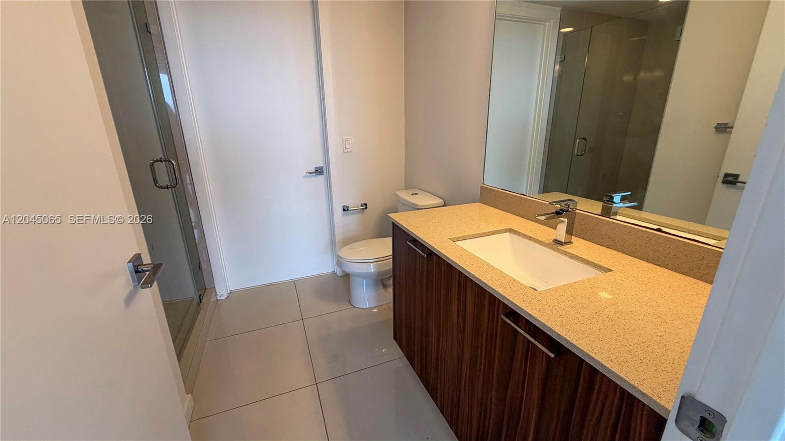 A modern bathroom features a wood-grain vanity, a beige countertop, and a glass-enclosed shower — DORAL, FL