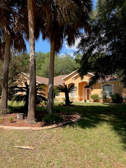A single-story tan house with a tiled roof is surrounded by palm trees and landscaping — 9273 SW 197TH CIR, DUNNELLON, FL