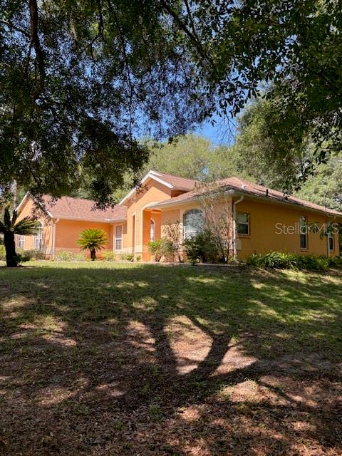 A single-story orange house with a shingled roof sits on a grassy, tree-shaded lot — 9273 SW 197TH CIR, DUNNELLON, FL
