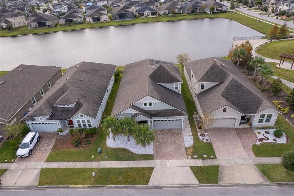 An aerial view shows three suburban houses with paved driveways facing a large retention pond — 3026 JARDIN STREET, KISSIMMEE, FL