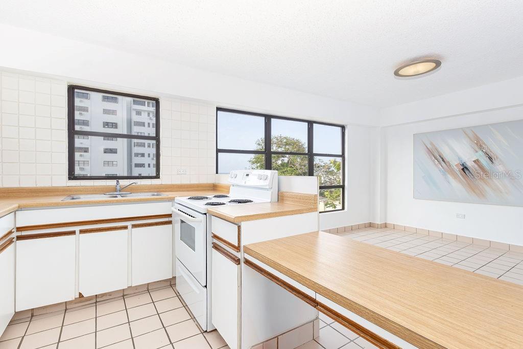 A kitchen with white cabinets, wood-look laminate countertops, tile flooring, and two large windows — 277 SAN JORGE UNIT 202, SAN JUAN, PR