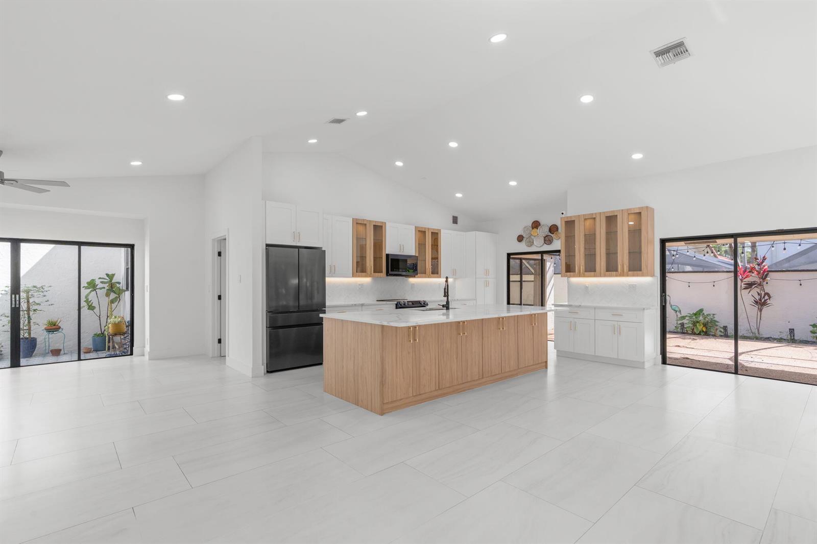 A modern kitchen features a large wood-toned island, white cabinetry, and sliding glass patio doors — 21326 Campo Allegro Drive, Boca Raton FL 33433, BOCA RATON, FL