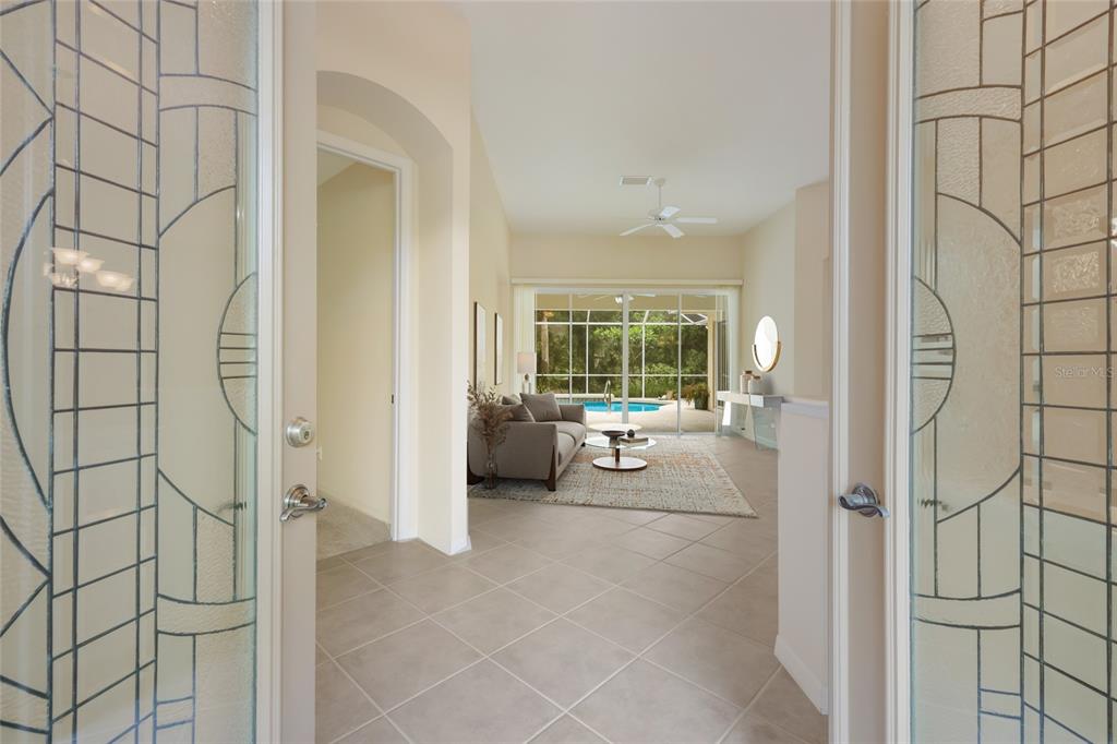 A view through glass-paned doors into a living room with tile floors and a pool — 8005 WATERVIEW BOULEVARD, LAKEWOOD RANCH, FL