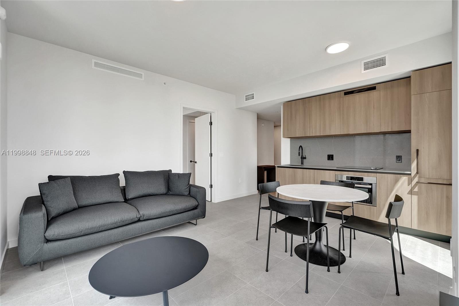 A modern open-concept living area features a gray sofa, dining table, and light wood cabinetry — 121 NE 5th ST # 2101, Miami FL 33132, MIAMI, FL